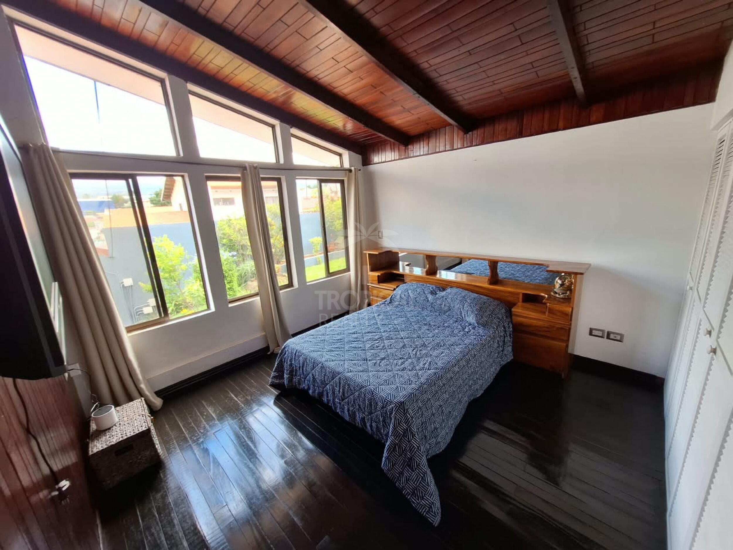 Dormitorio con cielo de madera y ventanales hacia el jardín